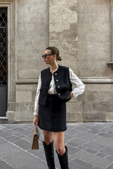 a lady in a white ruffle collared shirt, a black tweed vest and a black tweed skirt